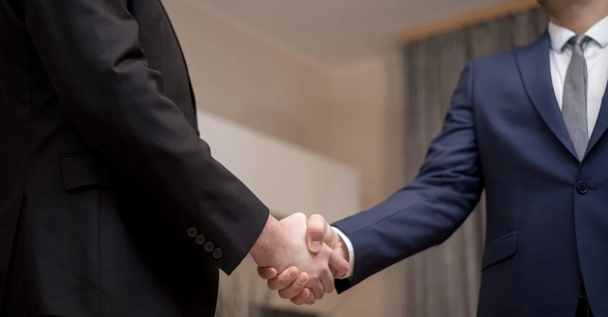 Deux hommes d'affaires en costumes se serrant la main, soulignant la confiance et le partenariat à l'intérieur.