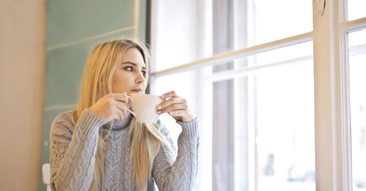 Une femme aux cheveux blonds savoure un café chaud dans un café intérieur confortable.