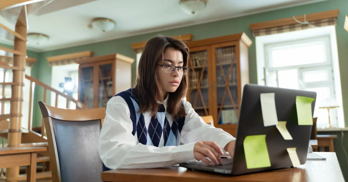 Jeune femme étudiant intensément sur un ordinateur portable dans une bibliothèque universitaire.